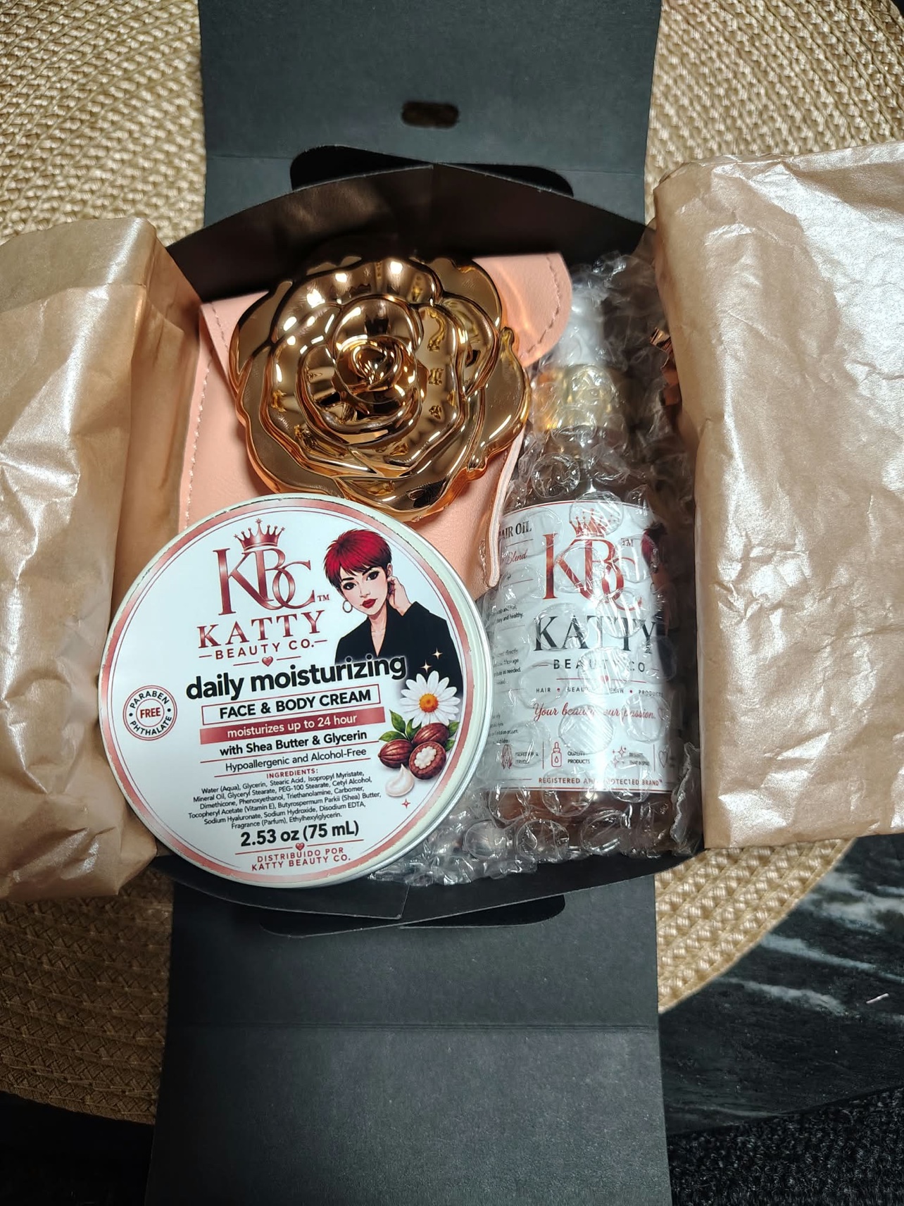 Cajita de regalo KBC abierta con crema hidratante, Scalp & Hair Oil y espejo de rosa dorada